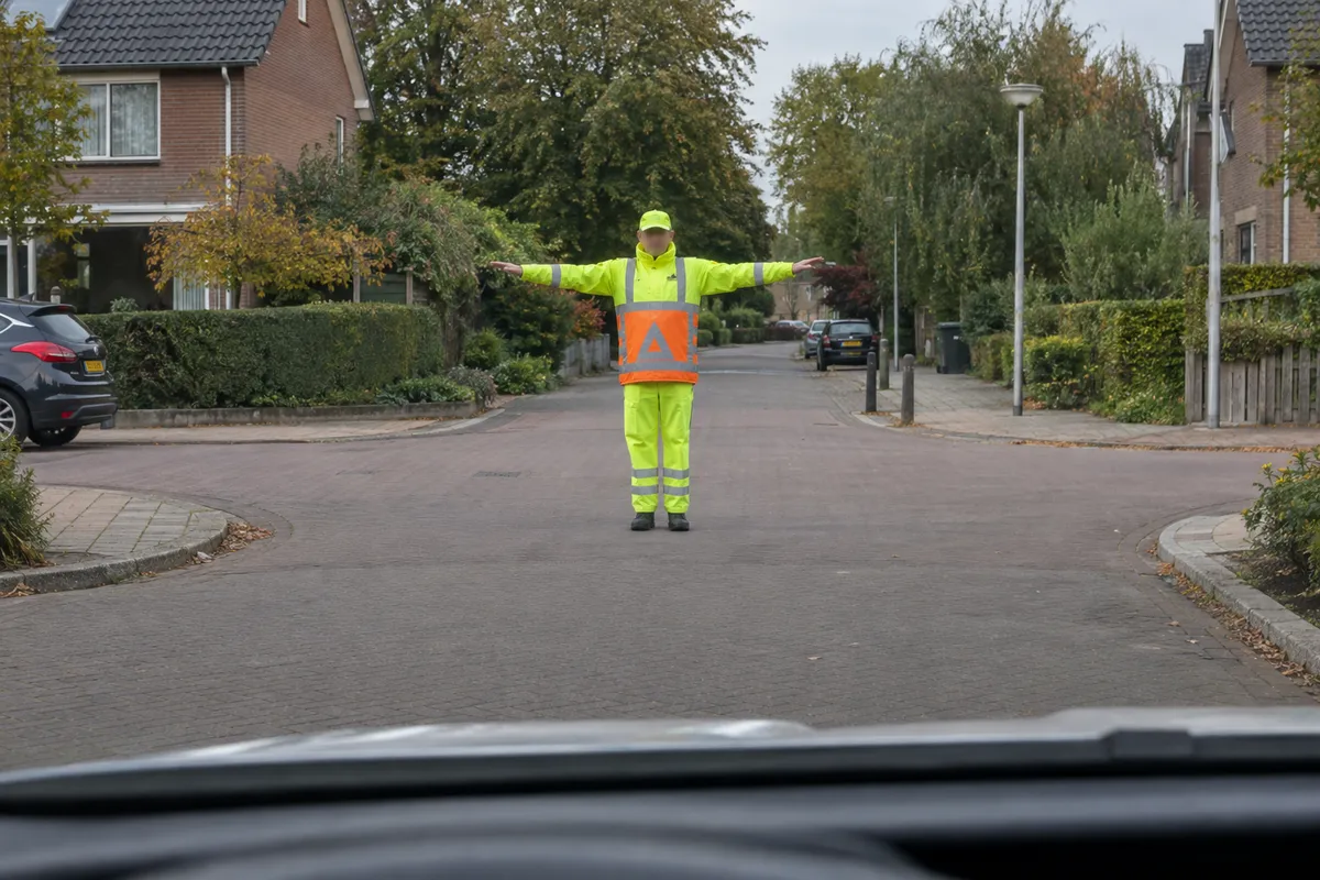 Een verkeersregelaar staat tegenover je met beide armen horizontaal opzij gestrekt.