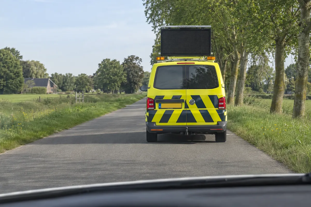 Vanuit je auto zie je het verlichte stopteken op het voertuig van een weginspecteur voor je.
