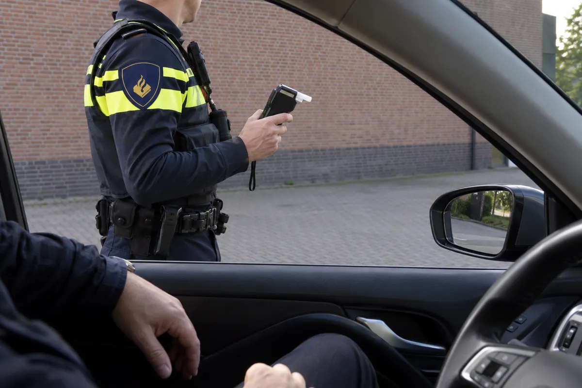Vanuit een stilstaande auto zie je een politieambtenaar met een ademtestapparaat voordat het onderzoek begint.