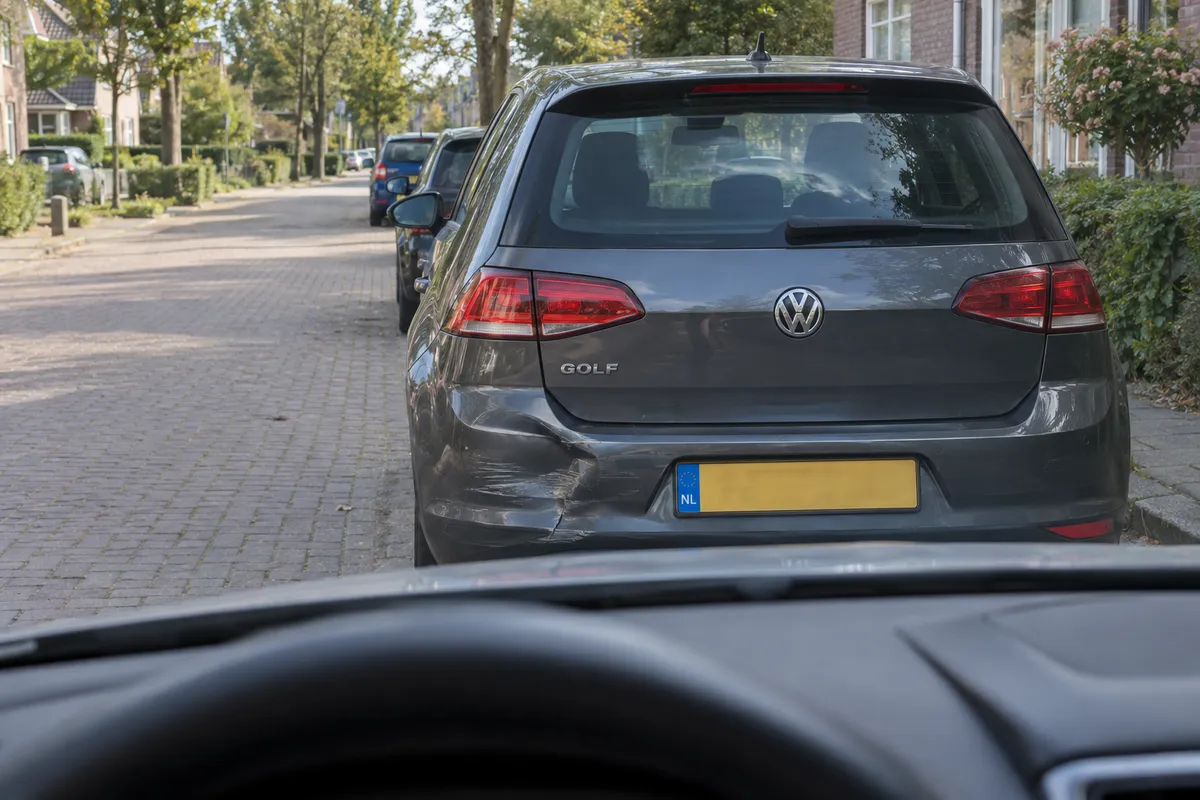 Vanuit je stilstaande auto zie je een geparkeerde auto met een kleine deuk en krassen na licht contact.