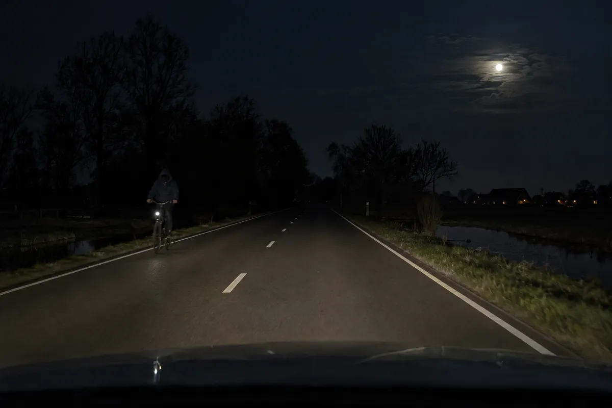 Op een donkere weg nadert een fietser uit de tegenovergestelde richting.