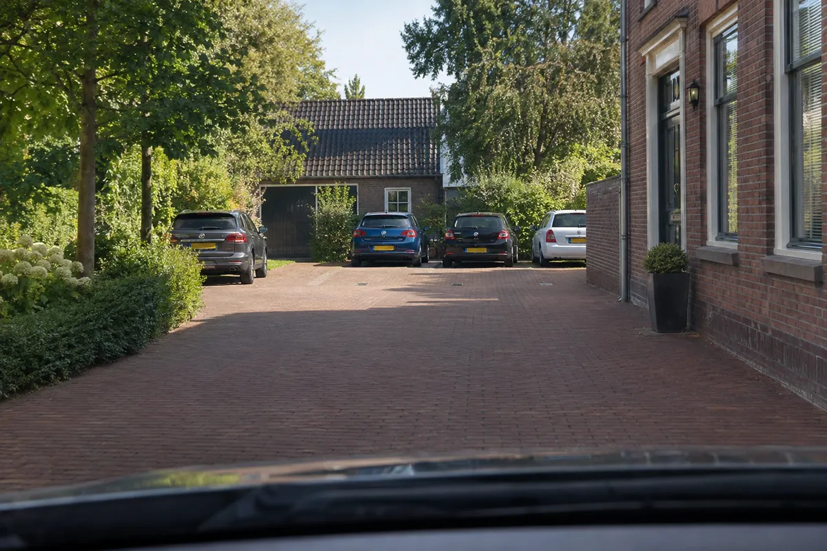 Zicht vanuit de auto in een erf: vooraan een vrije strook zonder markering langs een huis, verderop drie plekken met een tegel met een P.