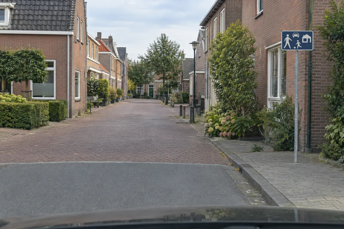 Je nadert met de auto de ingang van een erf. Het bord Erf staat rechts, nog vóór je het gebied inrijdt.