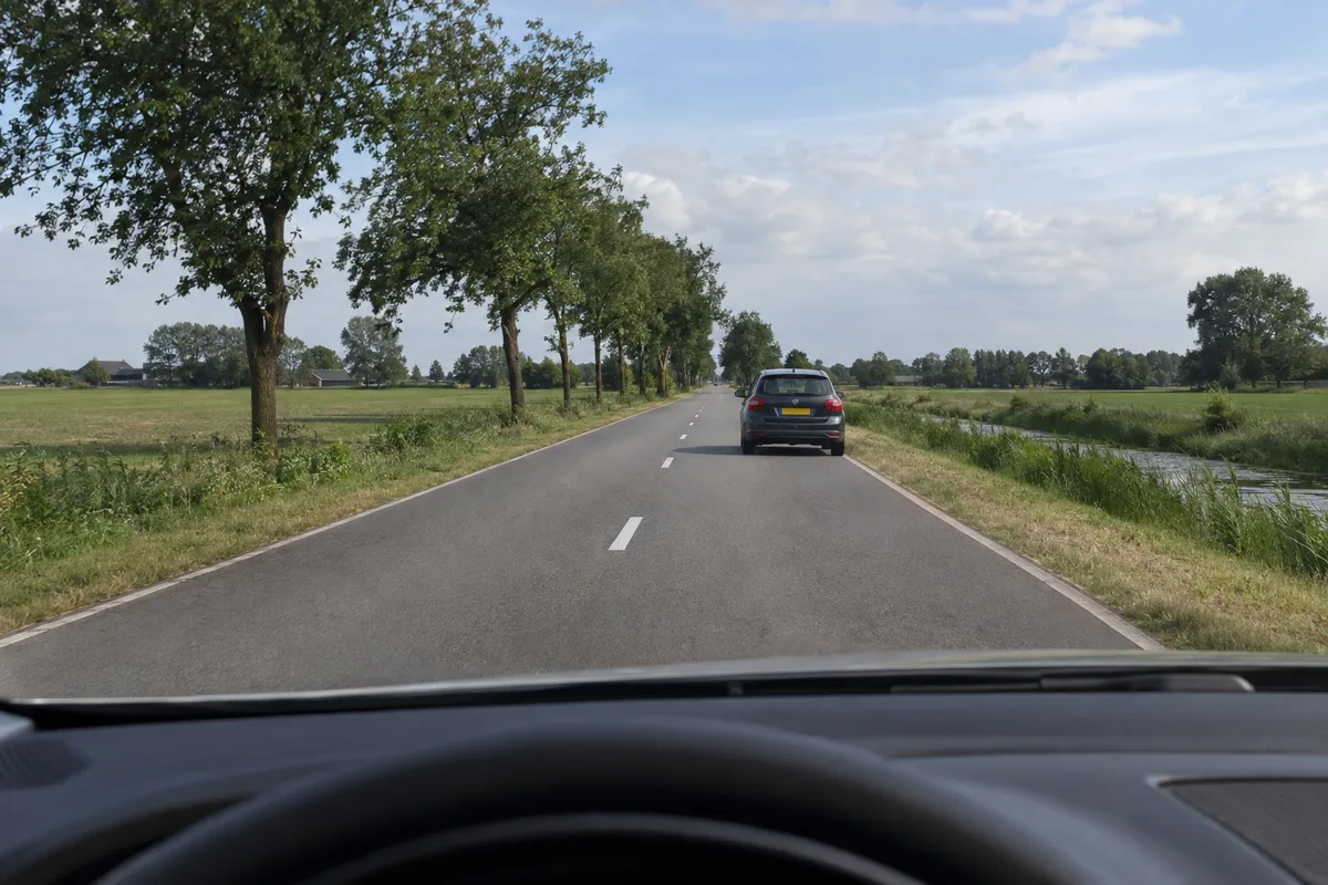Verderop staat een auto stil op jouw rijstrook en daarachter is de rechte weg nog zichtbaar.