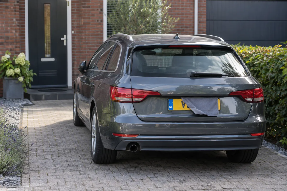 Een hoes hangt nog gedeeltelijk voor de achterste kentekenplaat van een geparkeerde auto.