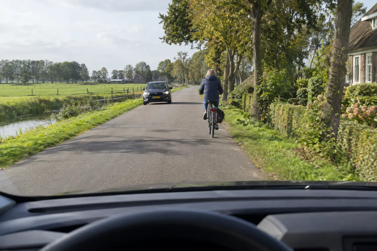 Een fietser rijdt voor onze auto op een smalle weg terwijl een auto uit de andere richting nadert.