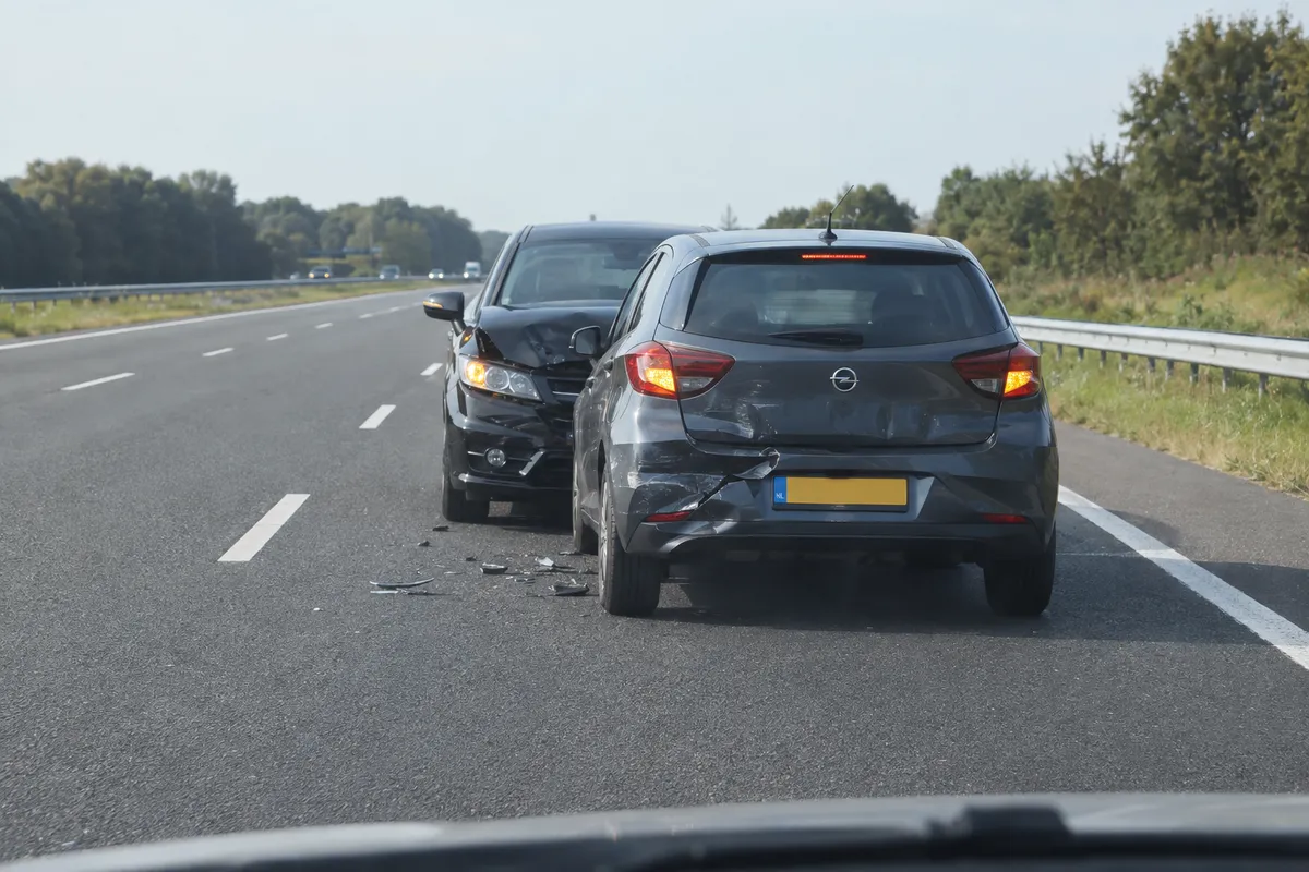 Na een ongeval staan de auto's stil. Naast de weg liggen een berm en een vangrail; de inzittenden zijn nog binnen.