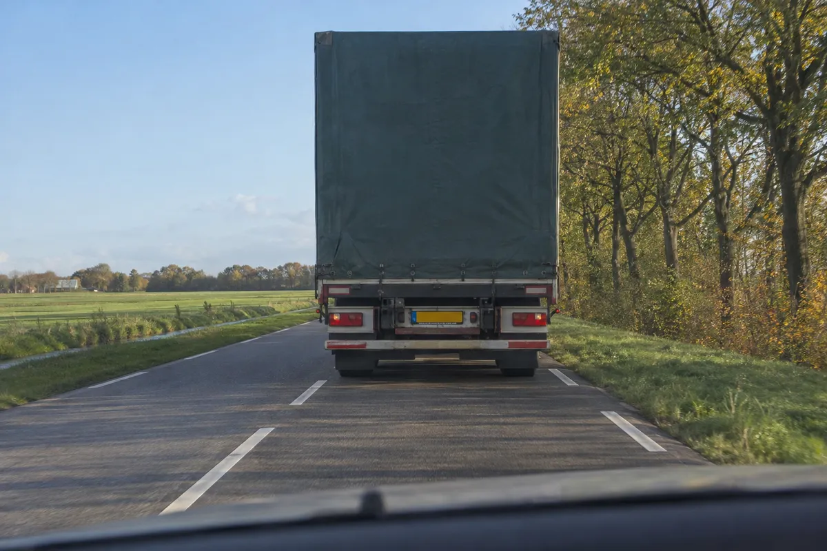 Zicht vanuit de auto op een weg: voor je rijdt een vrachtauto die het zicht op de weg afsluit