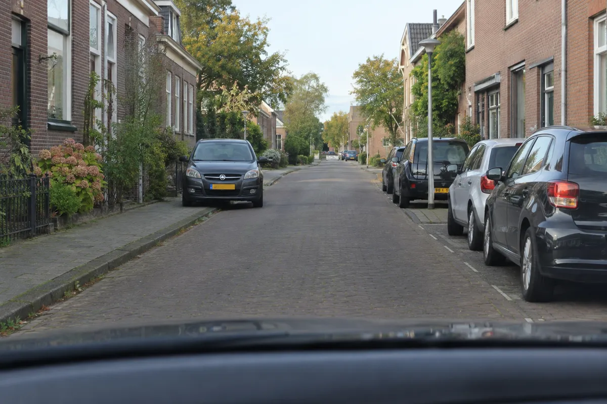 Zicht vanuit de auto in een smalle straat: een tegenligger is aan zijn kant gestopt om jou te laten passeren; jouw rijstrook is vrij.