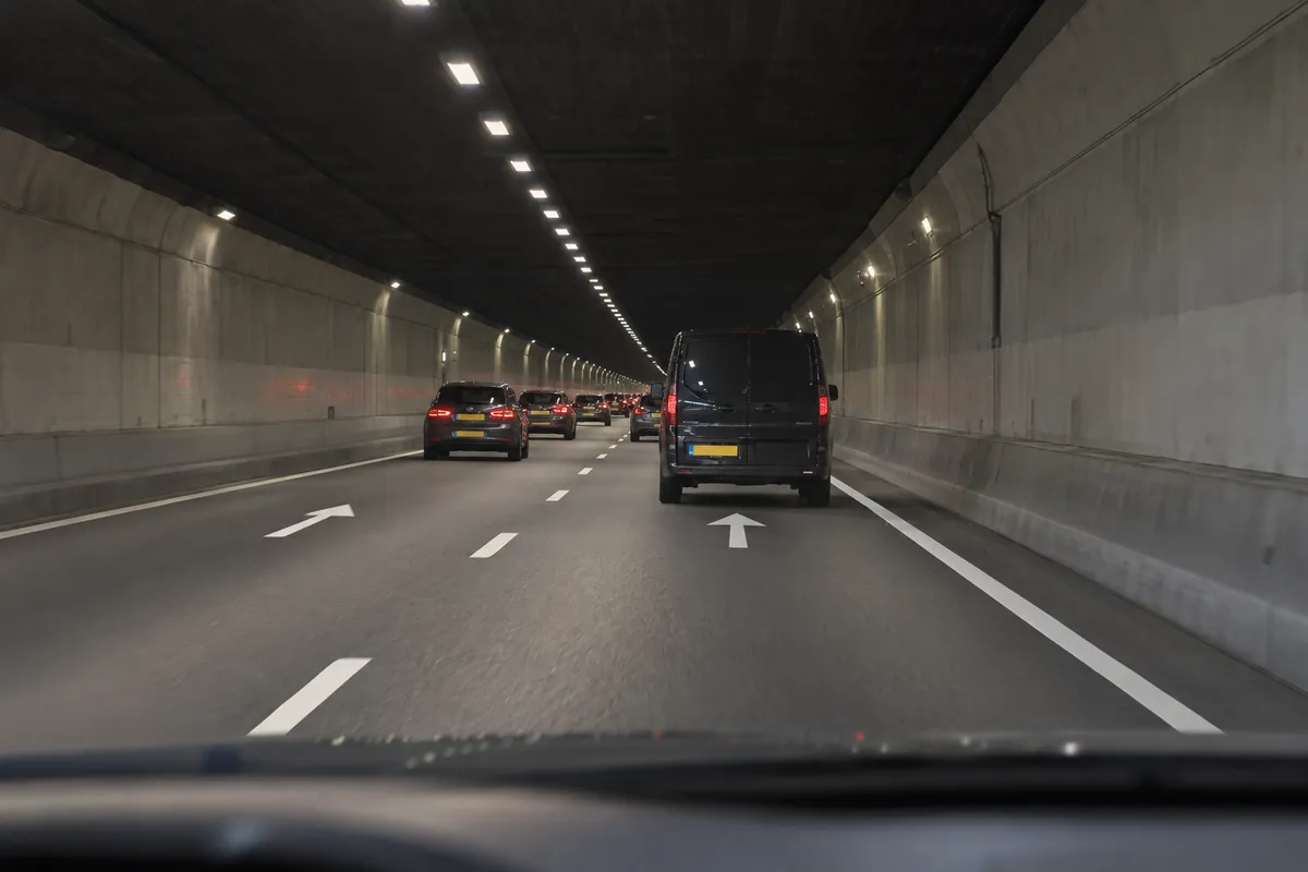 Je rijdt op de rechterrijstrook achter een bestelauto, met verkeer verderop in de tunnel.