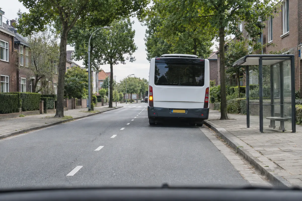 Zicht vanuit de auto op een bus die bij een halte in een stadsstraat staat, met knipperende richtingaanwijzer
