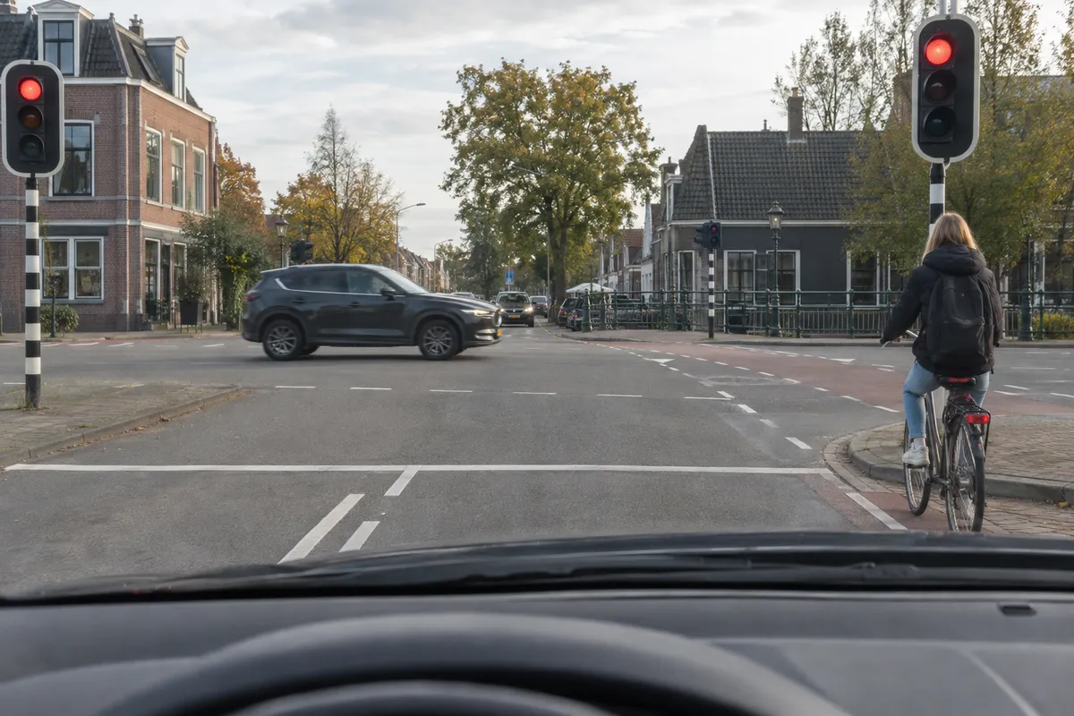 Je wacht voor rood terwijl rechts naast je een fietser vóór de afslag staat.
