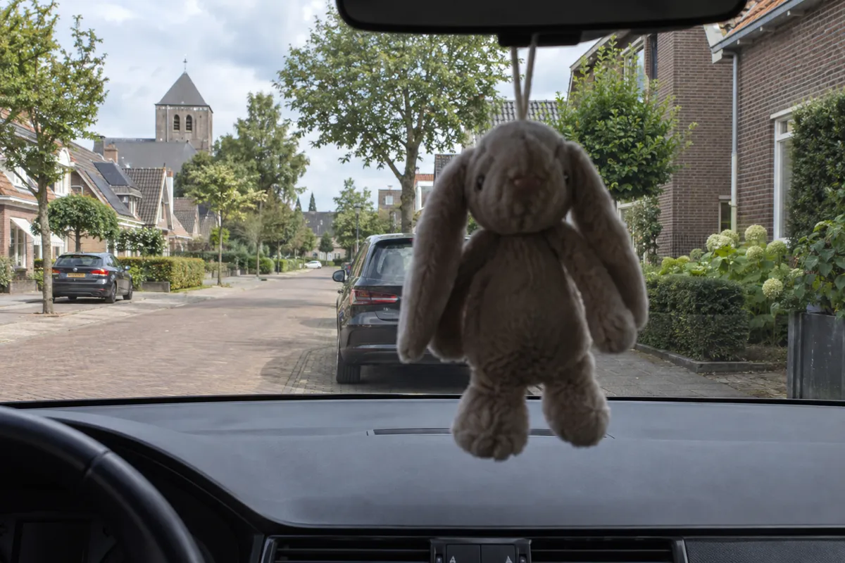 Vanuit de bestuurdersstoel van een geparkeerde auto blokkeert een groot hangend voorwerp een deel van het zicht op de straat.