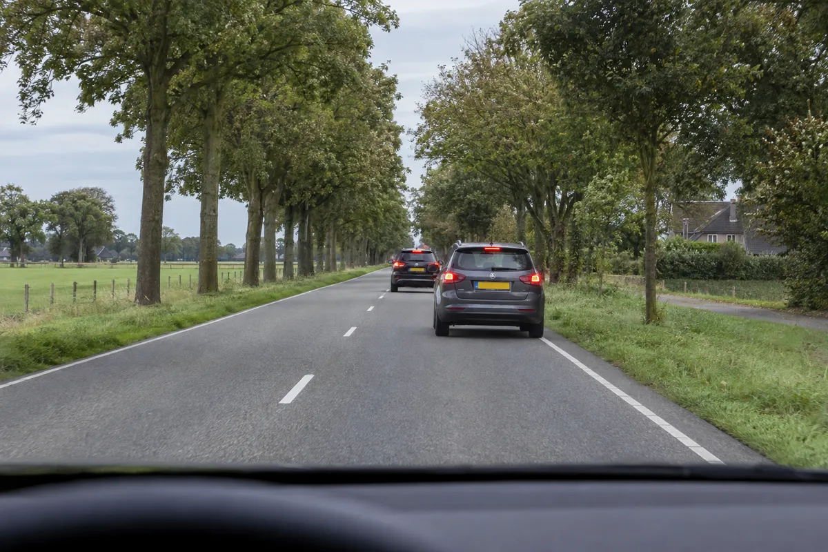 Voor je rijden twee auto's met brandende remlichten op een weg met één rijstrook per richting.