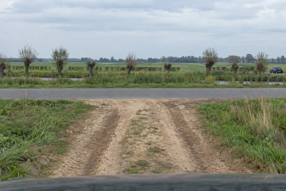 Zicht vanuit de auto op het eind van een zandweg: vlak voor de auto loopt een asfaltweg dwars door