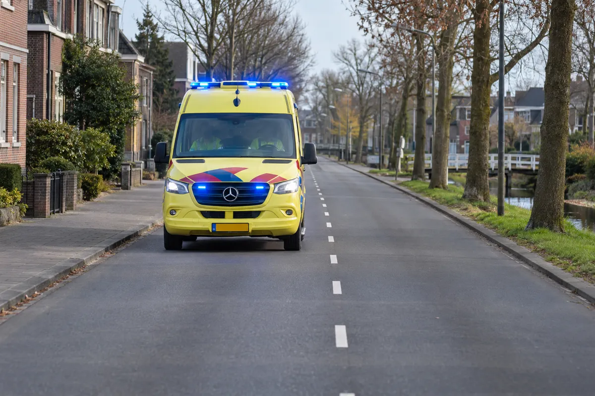 Een ambulance van voren gezien, overdag, met blauw knipperlicht op het dak en aan de voorkant