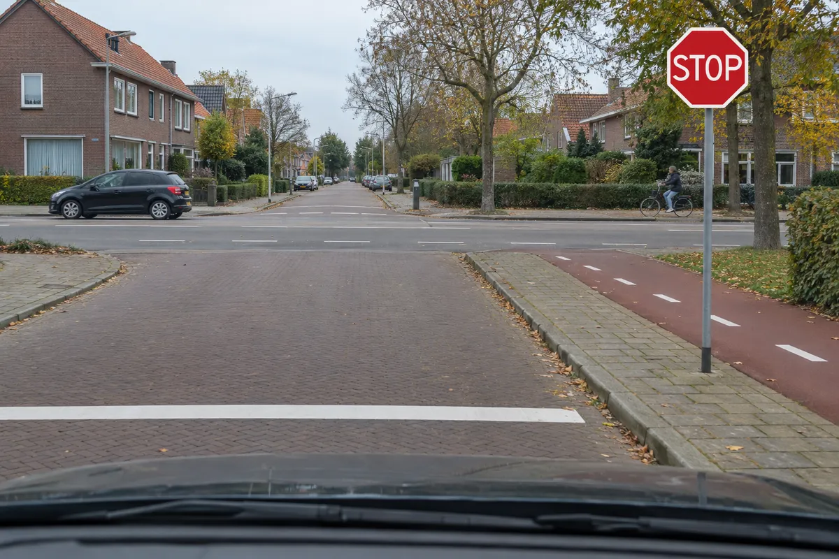 Zicht vanuit de auto op een zijweg: rechts staat het stopbord en vlak voor de auto ligt een stopstreep