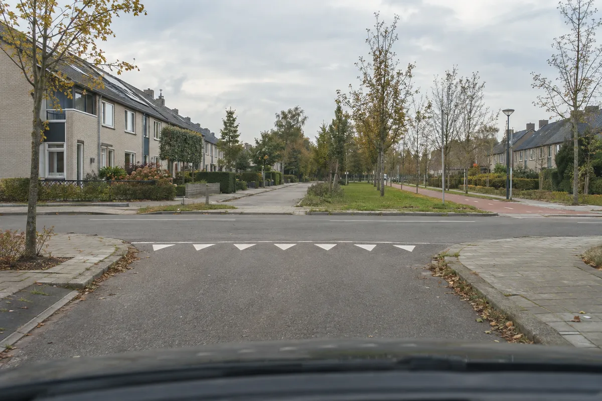 Zicht vanuit de auto op een zijweg: vlak voor het kruispunt liggen haaientanden op het wegdek