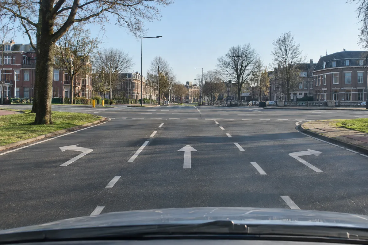 Zicht vanuit de auto op drie rijstroken vlak voor een kruispunt, met op elke strook een pijl op het wegdek