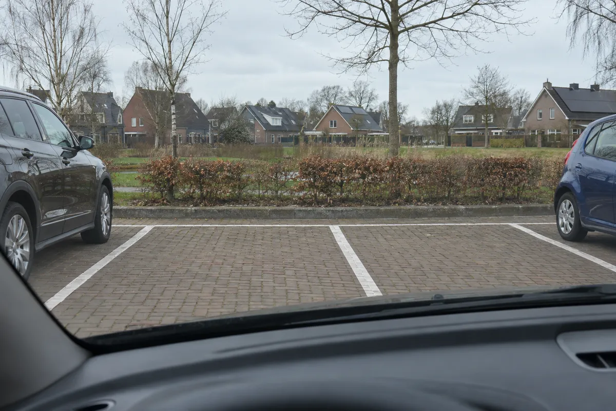 Vanuit een geparkeerde auto kijk je uit over een parkeerterrein.